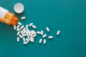 White pills scattered from an orange prescription bottle on a teal background.